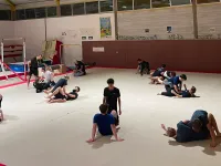 Pratiquants en tenue No Gi qui répètent une technique à deux sur le tatami, l’instructeur debout à côté d’un binôme
